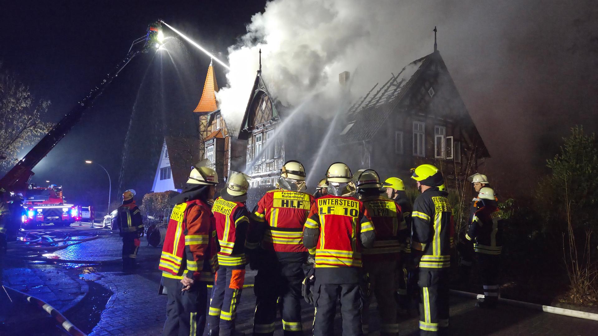 Feuerwehrleute in Schutzkleidung stehen vor einem Haus. Das Dach ist beschädigt, viel Rauch steigt auf. | Kreisfeuerwehr Rotenburg (Wümme)