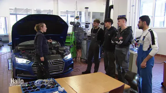 Kfz-Mechatronikerin Tabea Opitz erklärt ihren Auszubildenden etwas an einem Auto.