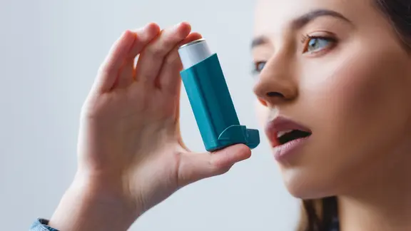 Eine junge Frau führt ein Asthmaspray zum Mund