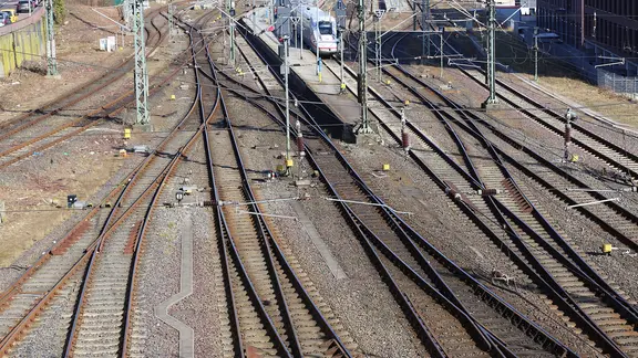 Oberleitungen mit Gleisen, im Hintergrund ein ICE.