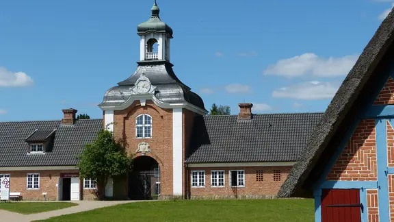 Ein Backsteintorbogen in der Sonne. Rechts vorne im Bild ist ein Teil eines Fachwerkhauses zu sehen