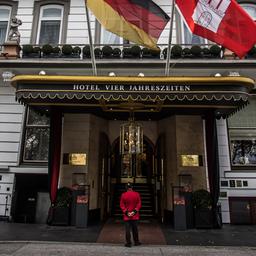 Haupteingang des Fairmont Hotel Vier Jahreszeiten in Hamburg. Davor steht ein Concierge im roten Sakko.