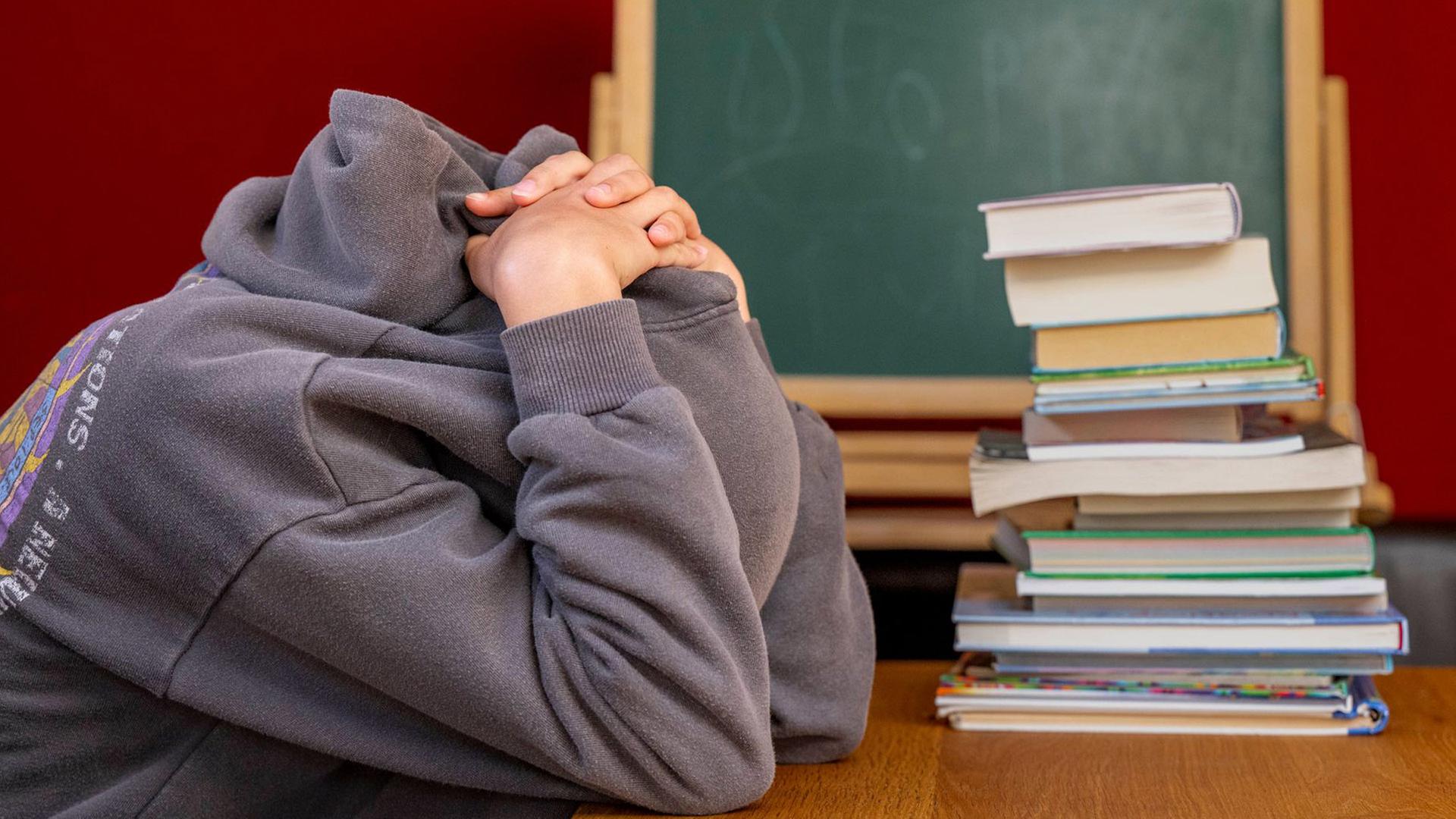 Ein Schüler verbirgt an einem Pult seinen Kopfe unter seinen Armen und Kapuze | David Inderlied/dpa