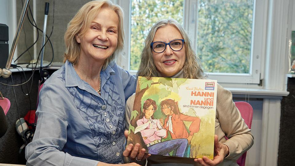 Sprecherin Manuela Dahm ist eines der Hörspielkinder, mit denen Heikedine Körting gearbeitet hat - in der Reihe "Hanni und Nanni" | picture alliance/dpa, Georg Wendt Heikedine Körting (l.), Produzentin, und Manuela Dahm, Sprecherin, sitzen am 13.11.2022 während eines Fototermins zu 50 Jahre "Hanni und Nanni"-Hörspiele im Tonstudio am Hamburger Rothenbaum. Die Enid-Blyton-Adaption über die frechen Zwillinge war die erste eigenproduzierte Serie der Hörspiel-Ikone Heikedine Körting.