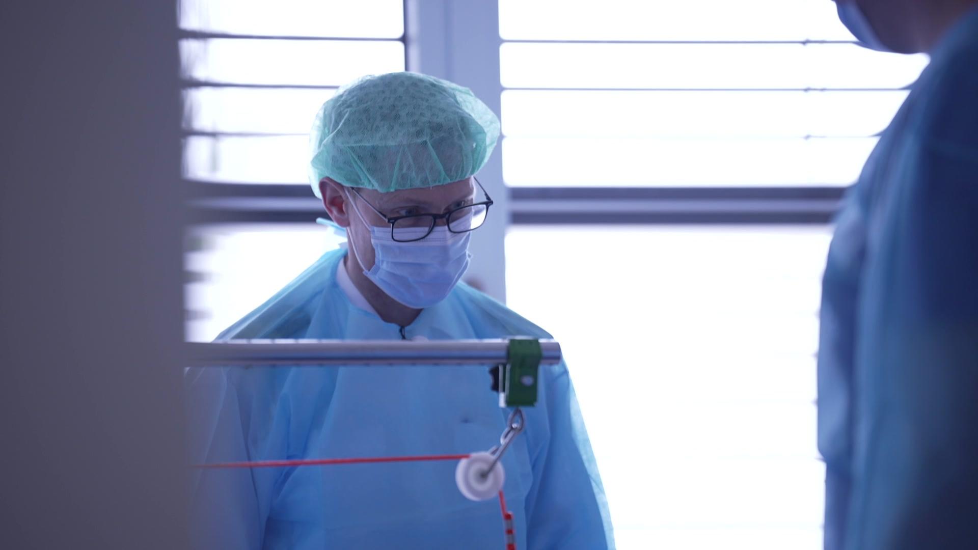 Ein Arzt steht in Kittel, mit OP-Haube und Maske in einem Krankenhaus. | NDR