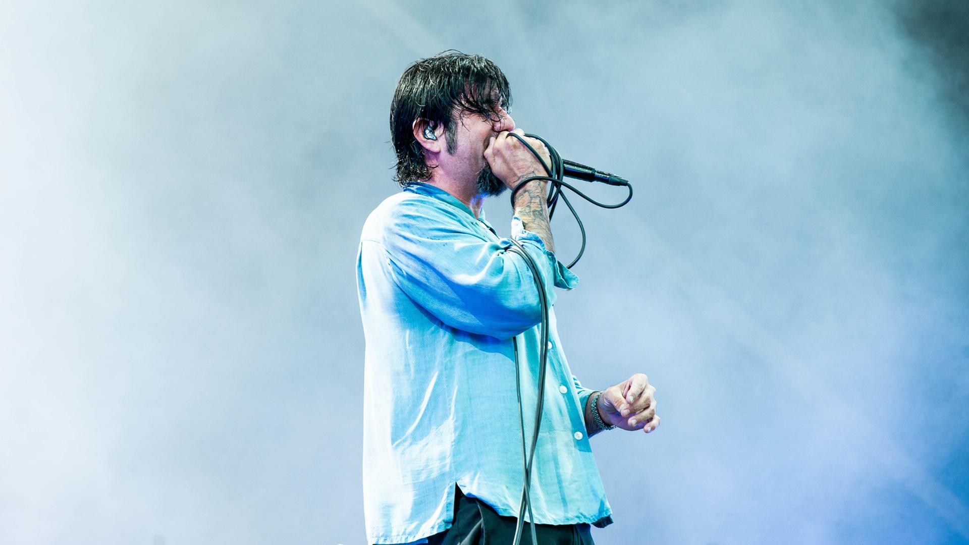Deftones-Sänger	 Chino Moreno steht vor eine Nebel-Wand und singt in ein Mikrofon.  | picture alliance / Photoshot | -