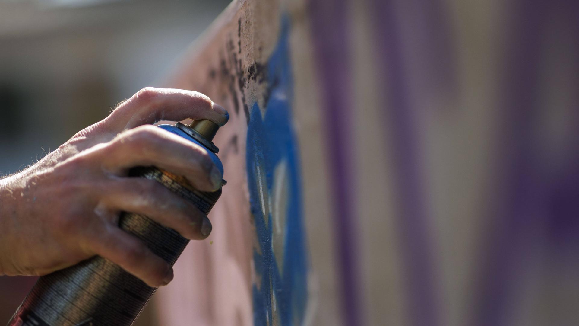 Eine Hand mit Spraydose vor einer mit Graffiti besprühten Wand. | imago images / photothek