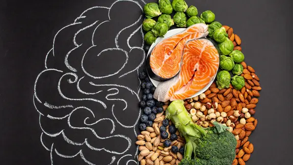 Gesunde Lebensmittel liegen auf einer Tafel. Daneben wurde ein halbes Gehirn mit Kreide gezeichnet.