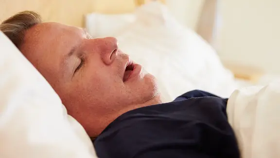 Ein schlafender Mann liegt mit offenem Mund und auf dem Rücken in einem Bett | colourbox Ein schlafender Mann liegt mit offenem Mund und auf dem Rücken in einem Bett