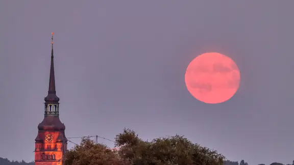 Frank Kossiski aus Itzehoe (Kreis Steinburg) beobachtet mit der Kamera, wie der Supermond am Himmel aufsteigt und sich neben dem Kirchturm der Laurentii-Kirche "von seiner schönsten Seite" zeigt. | Frank Kossiski, Frank Kossiski Der rote Supermond steht am Himmel hinter einer Kirche in Itzehoe.