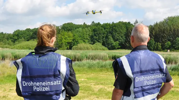 Zwei Polizisten des Drohnenteams stehen auf einer Wiese nahe der Oste. | Polizei Rotenburg Zwei Polizisten des Drohnenteams stehen auf einer Wiese nahe der Oste.