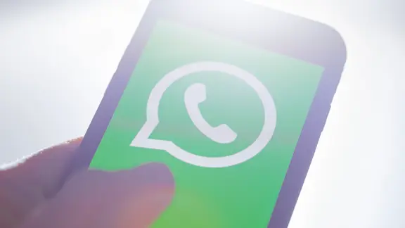 Eine Hand hält ein Smartphone mit der WhatsApp-App. 
