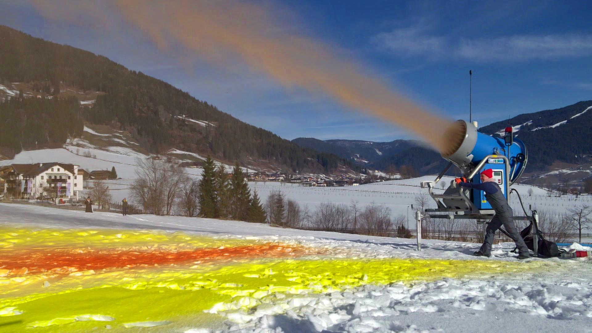 Eine Kanone feuert bunten Schnee auf einen Berg in den Alpen | Lisa Thierschmidt/NDR/arte