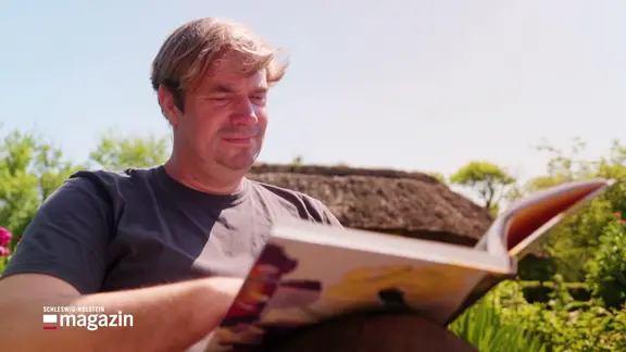 Ein Mann sitzt in einem Garten und liest ein Buch.