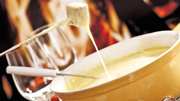 Ein Stück Brot wird in ein Käsefondue getunkt.