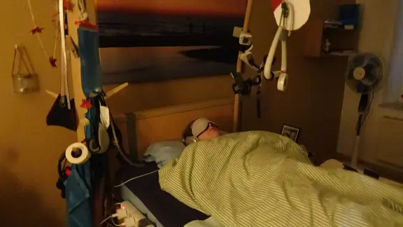 Eine Frau liegt in einem Bett und trägt eine Maske.