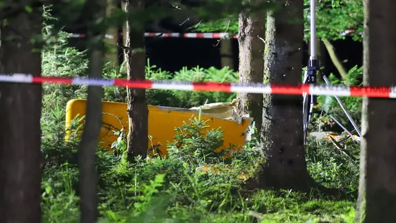 In einem Waldstück liegt ein Teil eines Flugzeugs, abgesperrt mit Flatterband.