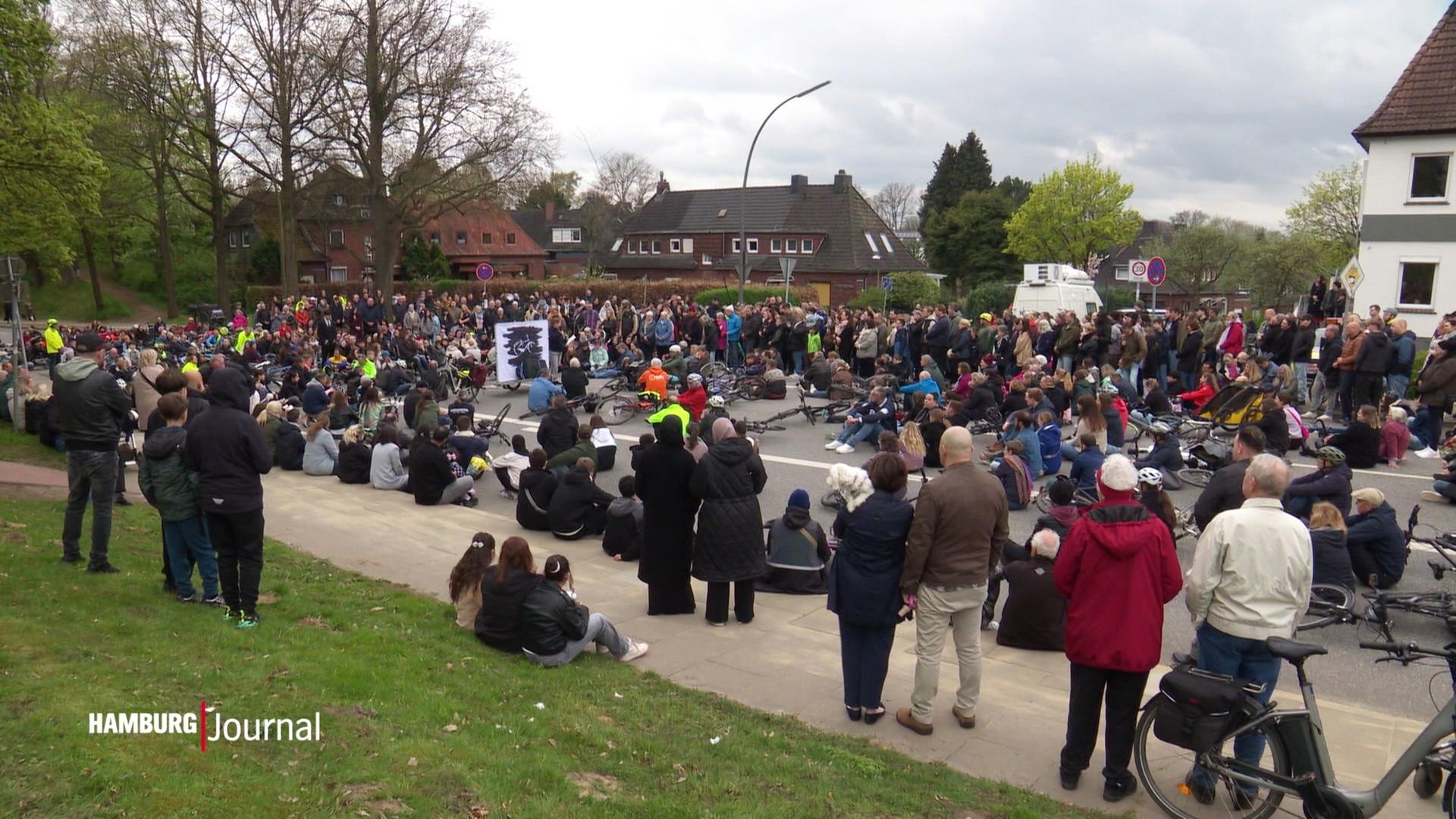 Viele Personen sitzen und stehen auf einer Straße, Fahrräder liegen auf der Straße. | Screenshot