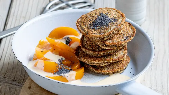 Ein Teller mit Pancakes, darauf einige Mohnsamen, daneben Aprikosenspalten.