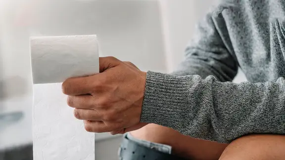 Mann sitzt auf Toilette, in seiner rechten Hand liegt eine Rolle Toilettenpapier (Bild: colourbox.de/Juan Moyano)
