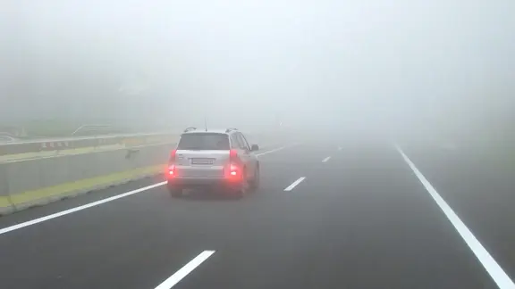 Ein Auto fährt bei Nebel mit eingeschalteter Nebelschlussleuchte.