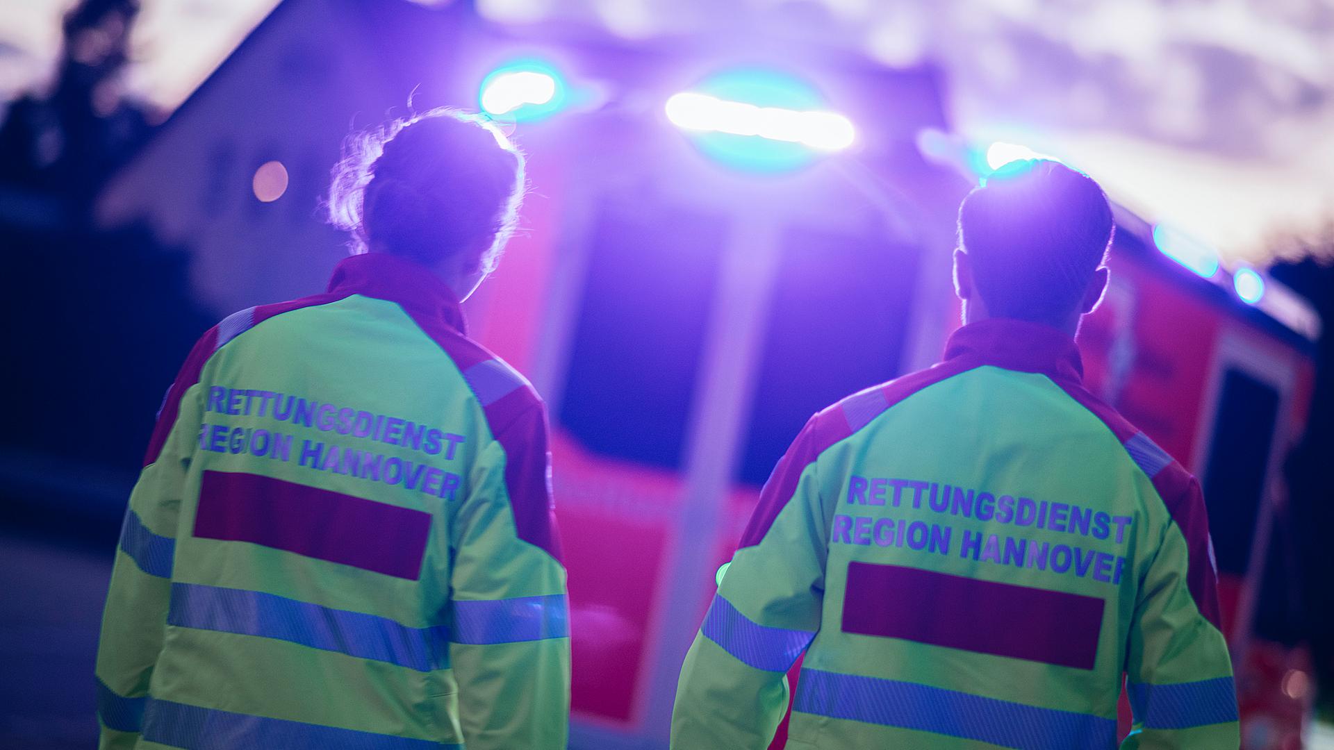 Zwei Sanitäter laufen zu einem Rettungswagen, der sie mit Blaulicht anstrahlt. | NDR, Julius Matuschik