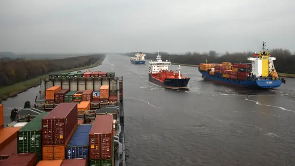 Mehrere Schiffe durchqueren den Nord-Ostsee Kanal unter grauem Himmel.