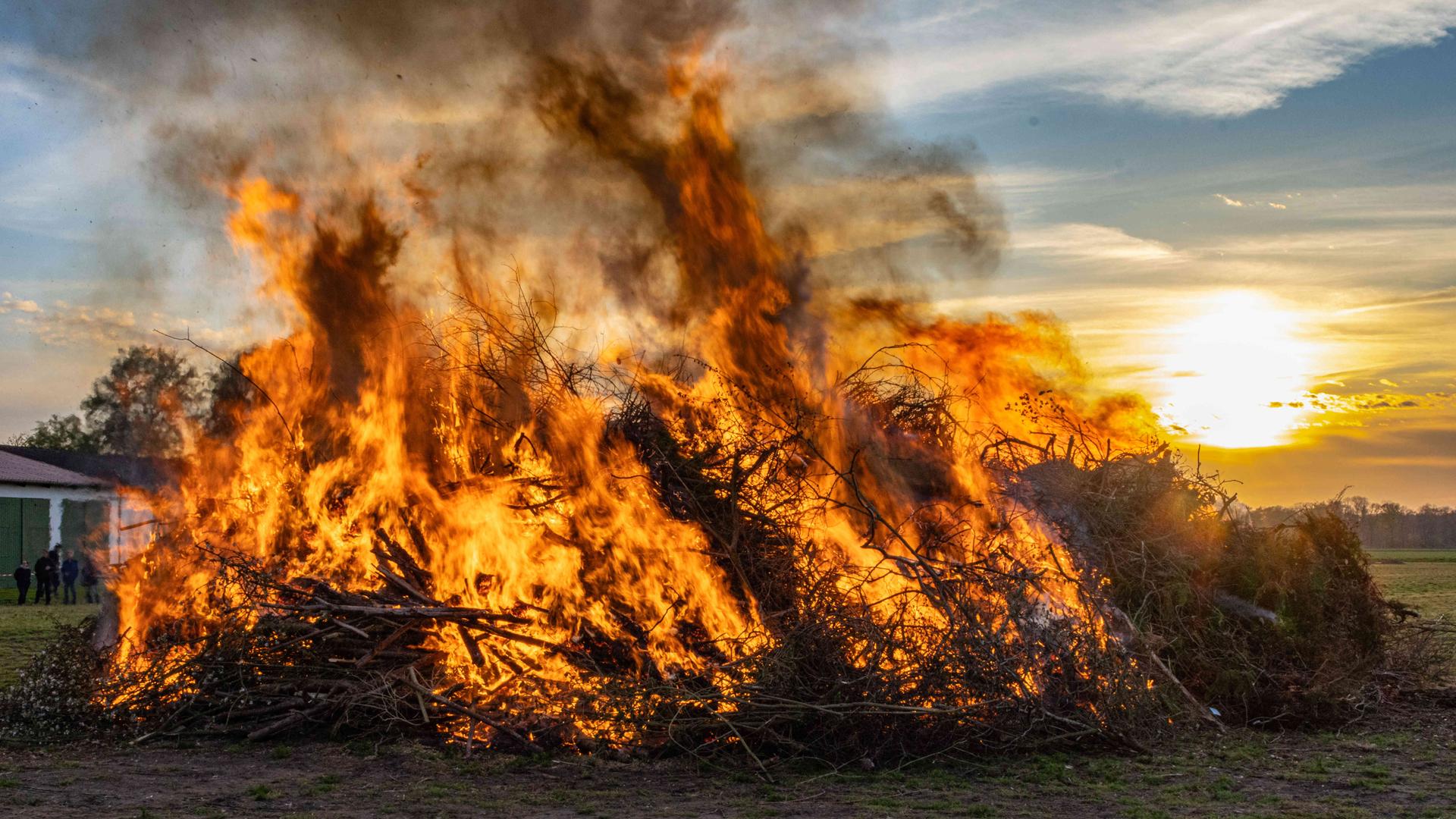 Ein großes Osterfeuer lodert bei Sonnenuntergang auf einer Wiese | picture alliance / Fotostand | Fotostand / Reiss