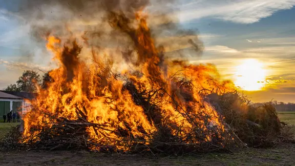 Ein großes Osterfeuer lodert bei Sonnenuntergang auf einer Wiese | picture alliance / Fotostand | Fotostand / Reiss Ein großes Osterfeuer lodert bei Sonnenuntergang auf einer Wiese