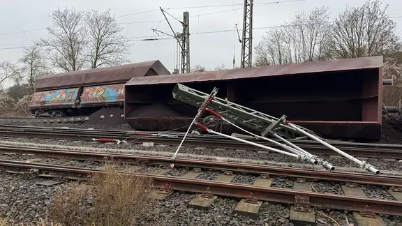 Ein Güterzug liegt auf Gleisen umgekippt auf der Seite neben einem umgekippten Mast.