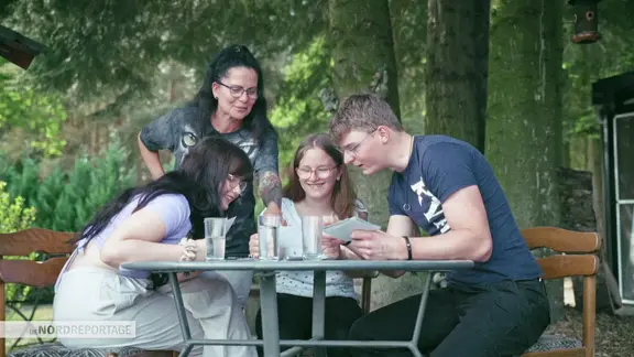 Eine Frau mit drei Kindern an einem Tisch im Freien. Sie schauen sich munter Bilder an.