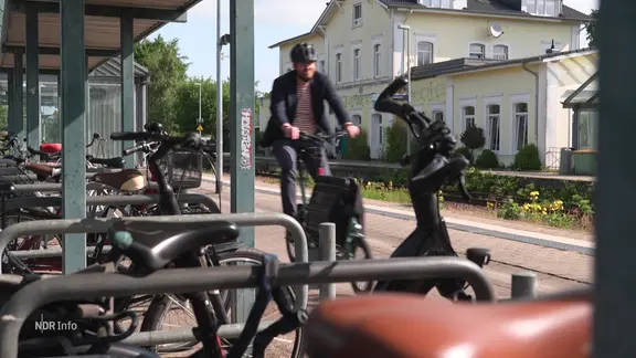 Ein Radfahrer fährt an einem überdachten Fahrradstellplatz mit vielen Fahrradständern vorbei.
