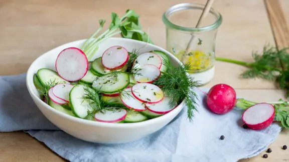 Gurken-Radieschen-Salat in einer Schüssel auf einem Holzbrett.