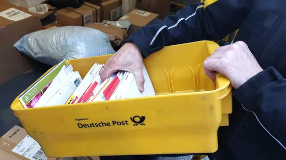 Ein Mann greift in einen Briefkasten voller Briefe