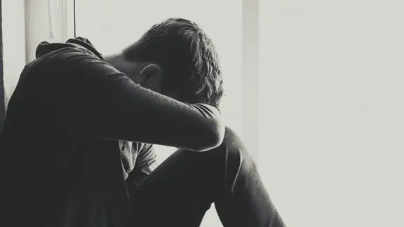 Ein junger Mann sitzt mit verborgenem Gesicht traurig am Fenster.