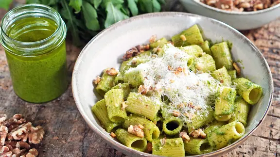 Ein tiefer Keramikteller mit Tortiglioni, Rucola-Pesto und gehackten Walnüssen