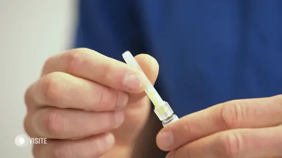 Eine Hand nimmt die Schutzkappe von einer Impfspritze ab.