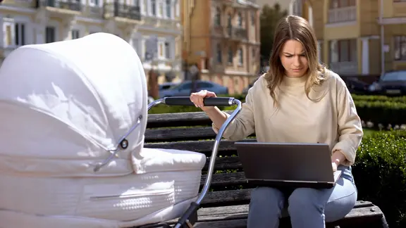 Mental Load: Junge Mutter kümmert sich um das Baby und arbeitet gleichzeitig.