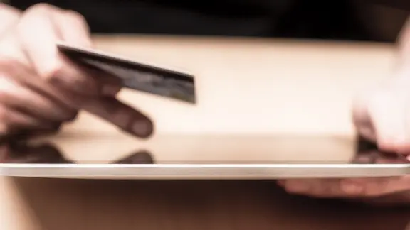 Eine Hand hält eine Bankkarte, die andere tippt auf einem Tablet. | Michael Zech Fotografie / photocase.de, Michael Zech Fotografie / photocase.de Eine Hand hält eine Bankkarte, die andere tippt auf einem Tablet.