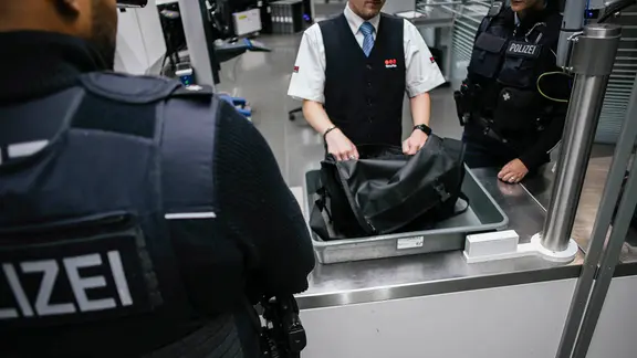 Zwei Beamte der Bundespolizei schauen sich in der Sicherheitskontrolle eines Flughafens ein verdächtiges Gepäckstück an.