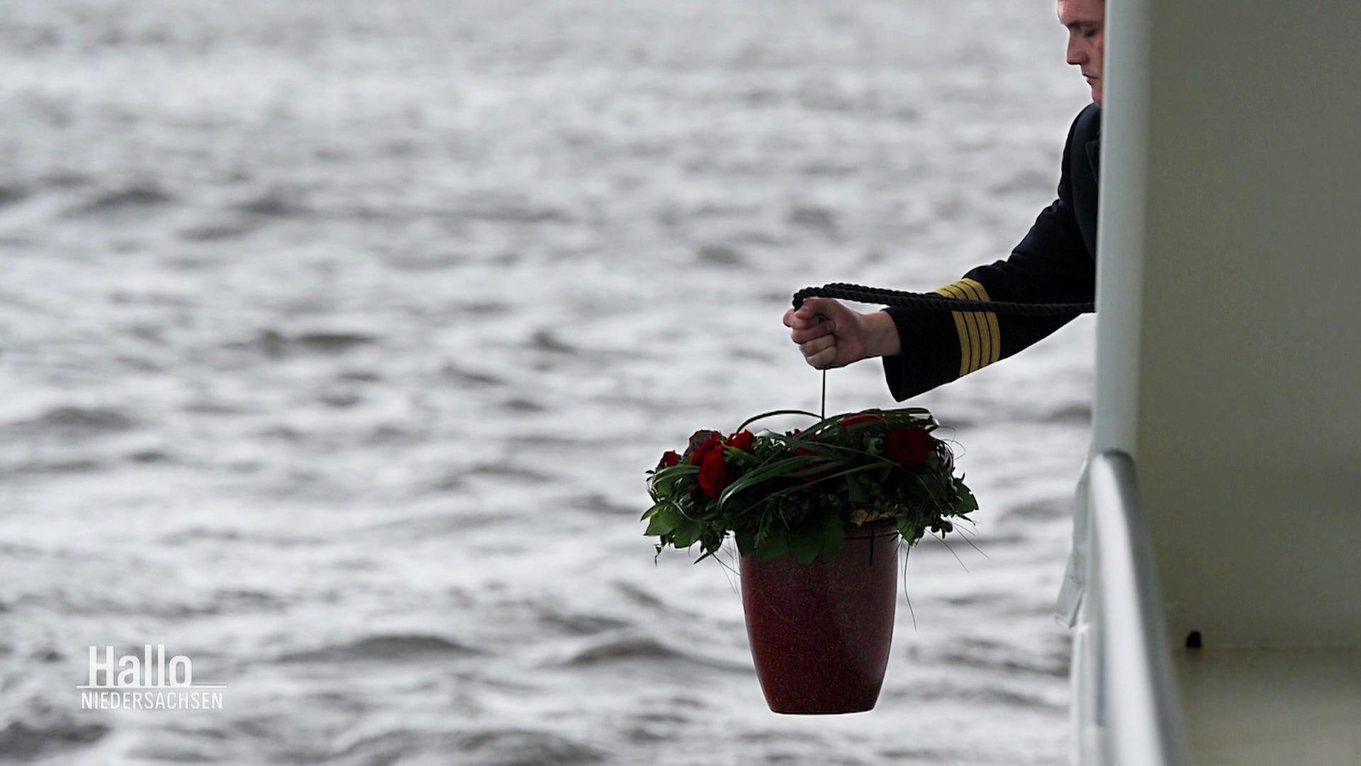 Eine Urne wird übers Wasser gehalten. | Screenshot