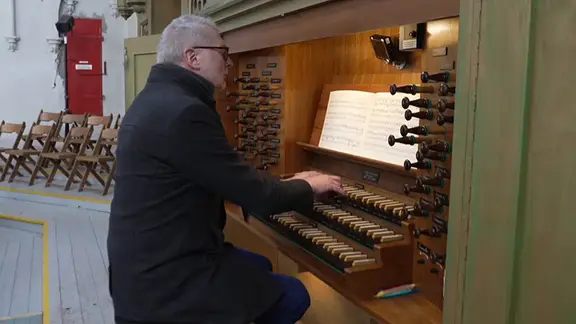 Mann sitzt an einer Orgel in einer Kirche