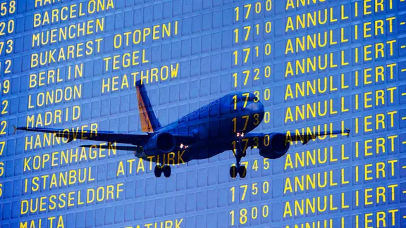 Eine Tafel am Flughafen zeigt mehrere ausgefallene Flüge. Durch die Anzeige schimmert ein Flugzeug hindurch. | Imago Images, imageBROKER/Lilly Eine Tafel am Flughafen zeigt mehrere ausgefallene Flüge. Durch die Anzeige schimmert ein Flugzeug hindurch.