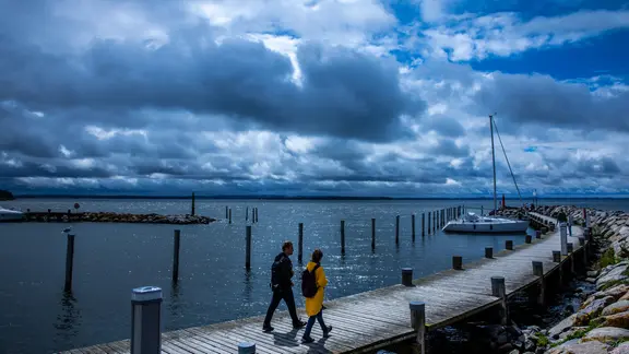 Spaziergänger sind vor einer dunklen Wolkenkulisse im Seglerhafen auf der Insel Poel unterwegs. 