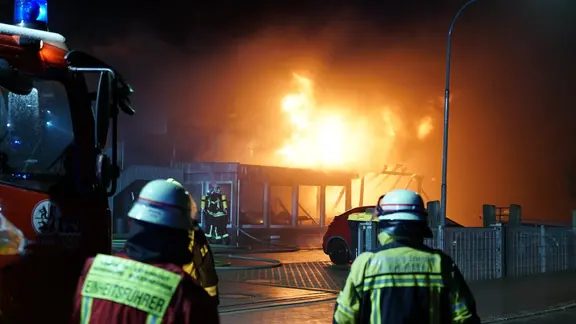 Mehrere Feuerwehrleute stehen vor einem Haus in Flammen