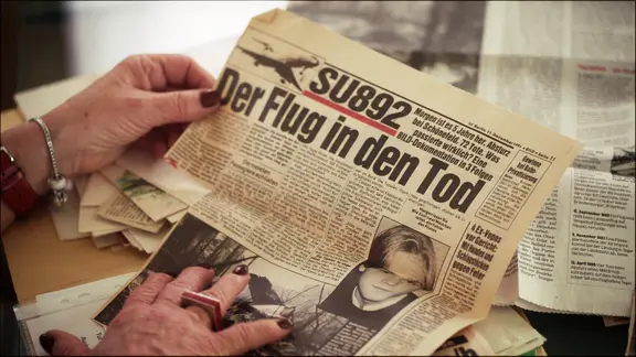 Ein Frau hält einen Zeitungsausschnitt mit dem Titel "Der Flug in den Tod".