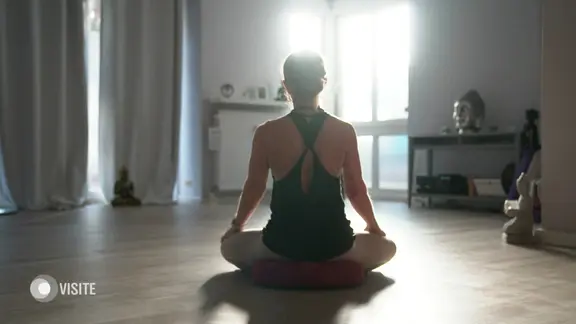 Eine Frau meditiert im Schneidersitz in einem Yoga-Studio.