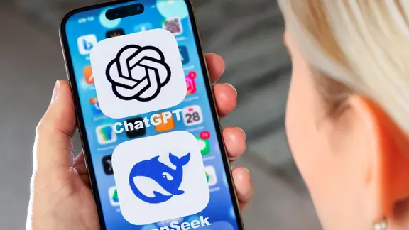 Eine Frau schaut auf das Display eines Handys, auf dem Bildschirm ist sind die beiden Symbole für die amerikanische KI-App ChatGBT und den chinesischen Konkurrenten DeepSeek zu sehen.
