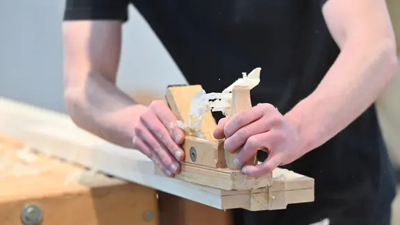 Ein Auszubildender schleift Holz ab.