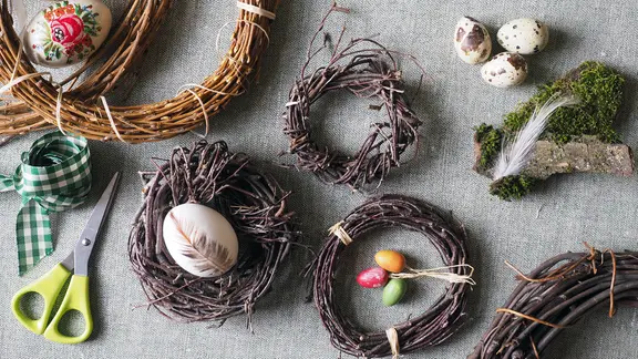 Verschieden Osterkränze und Bastelmaterial liegen auf einer Fläche.